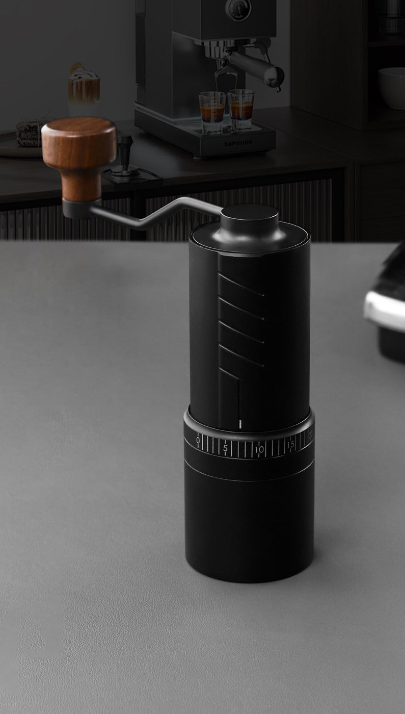 VEVOK CHEF O20 Manual Coffee Grinder standing on a table with an espresso machine in the background, demonstrating its compatibility with professional coffee-making equipment.
