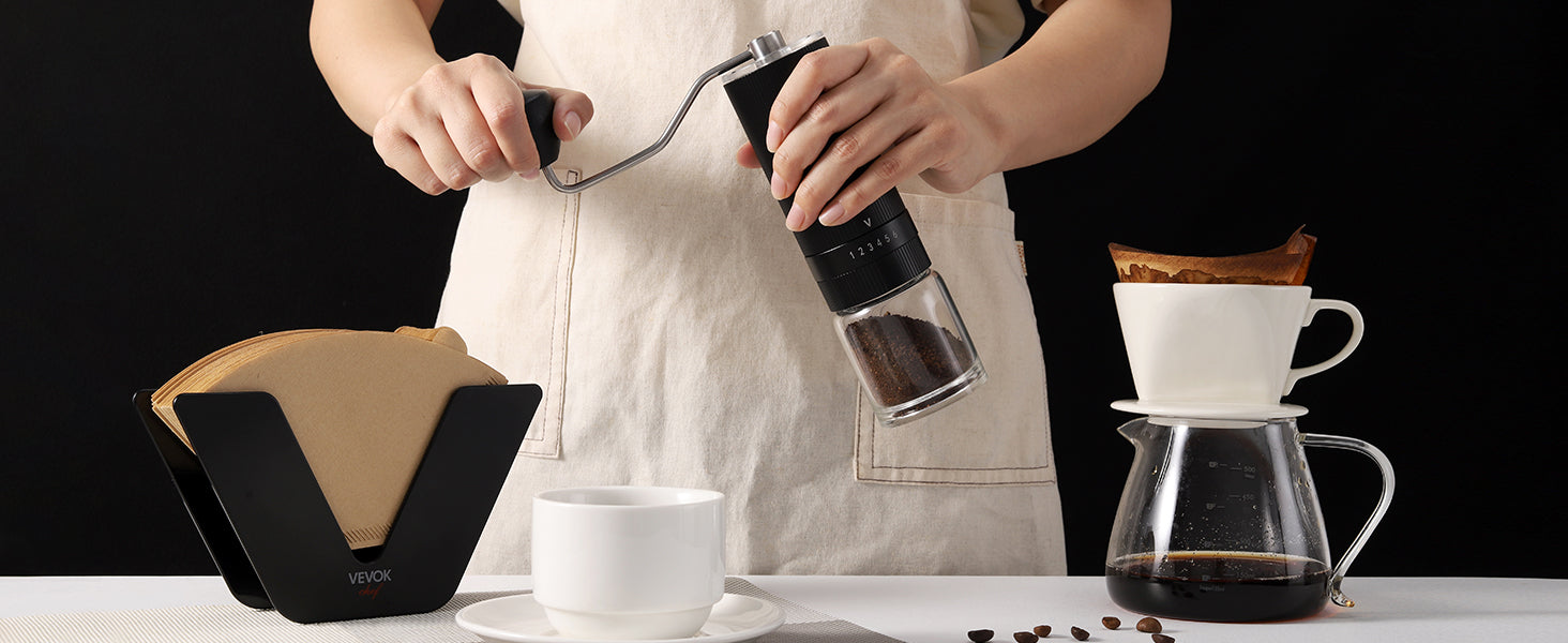 A barista standing behind a coffee counter, grinding coffee beans with the VEVOK CHEF O6 Slim Glass Manual Coffee Grinder, surrounded by pour-over brewing tools, emphasizing professional-level performance.