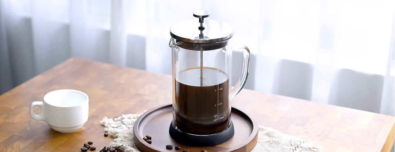 French press with coffee and a cup on a wooden table