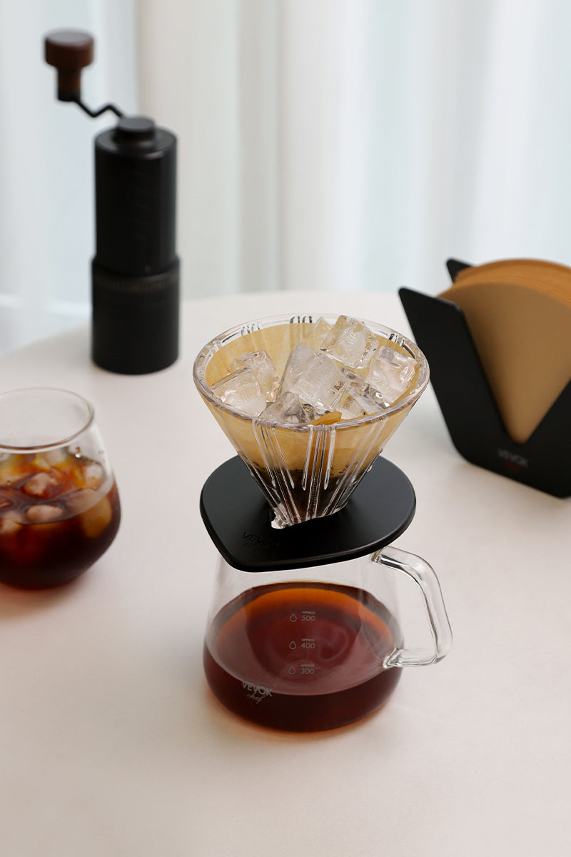 Preparing iced pour-over coffee with VEVOK CHEF hand brew kit, O20 grinder, filter holder, and an ice-filled glass on a white round table.
