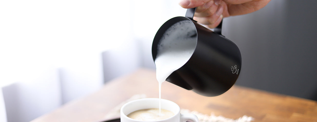 The VEVOK CHEF LARA Milk Frothing Pitcher pouring perfectly frothed milk into a coffee cup, showcasing its precision pouring and ideal design for creating professional latte art.