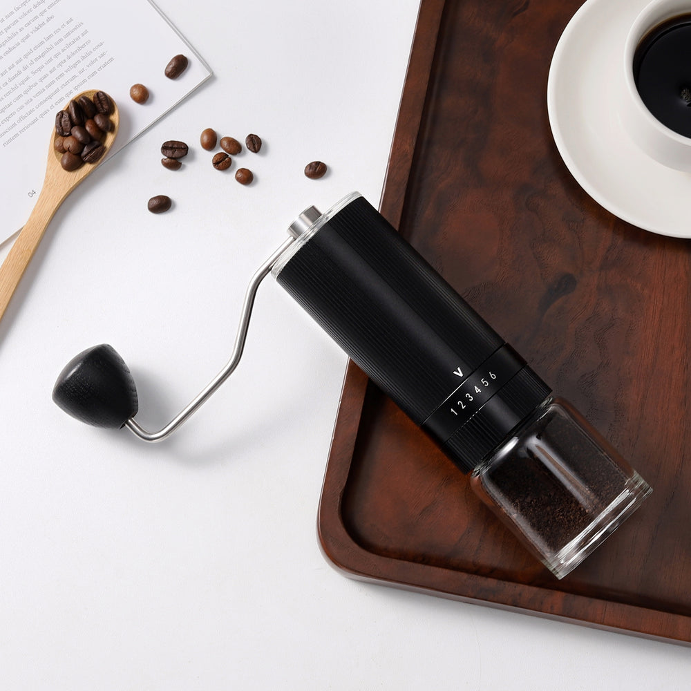 Top-down view of the VEVOK CHEF O6 Slim Manual Coffee Grinder Glass Jar, placed on a table with a wooden tray, coffee cup, and scattered coffee beans, showcasing its glass jar option with a stylish and functional design.

