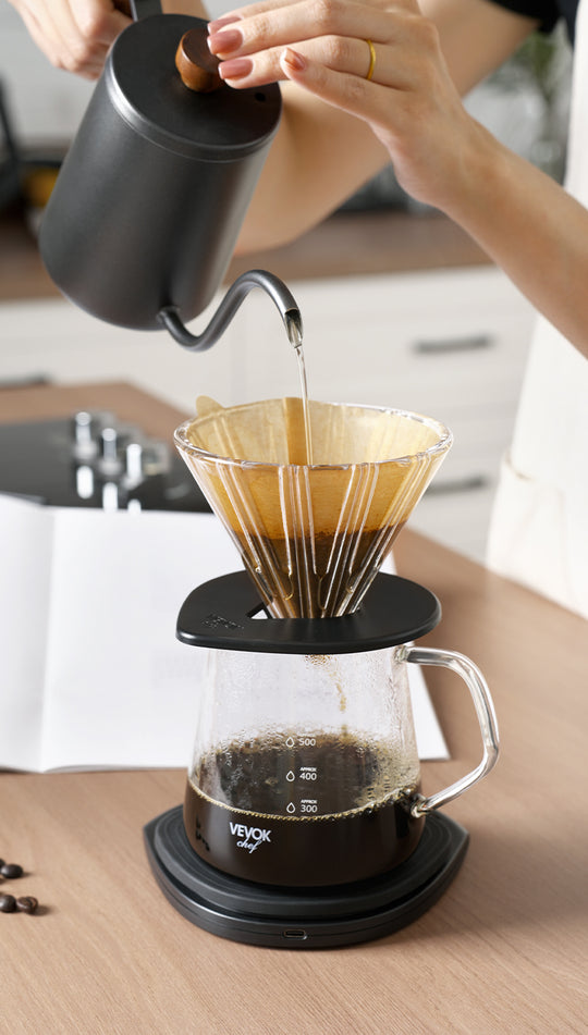 A home kitchen setup with the VEVOK CHEF Pour Over Coffee Maker Set as water from a long-spout kettle flows into the dripper. Coffee drips into the glass server below, showcasing the art of pour-over brewing.